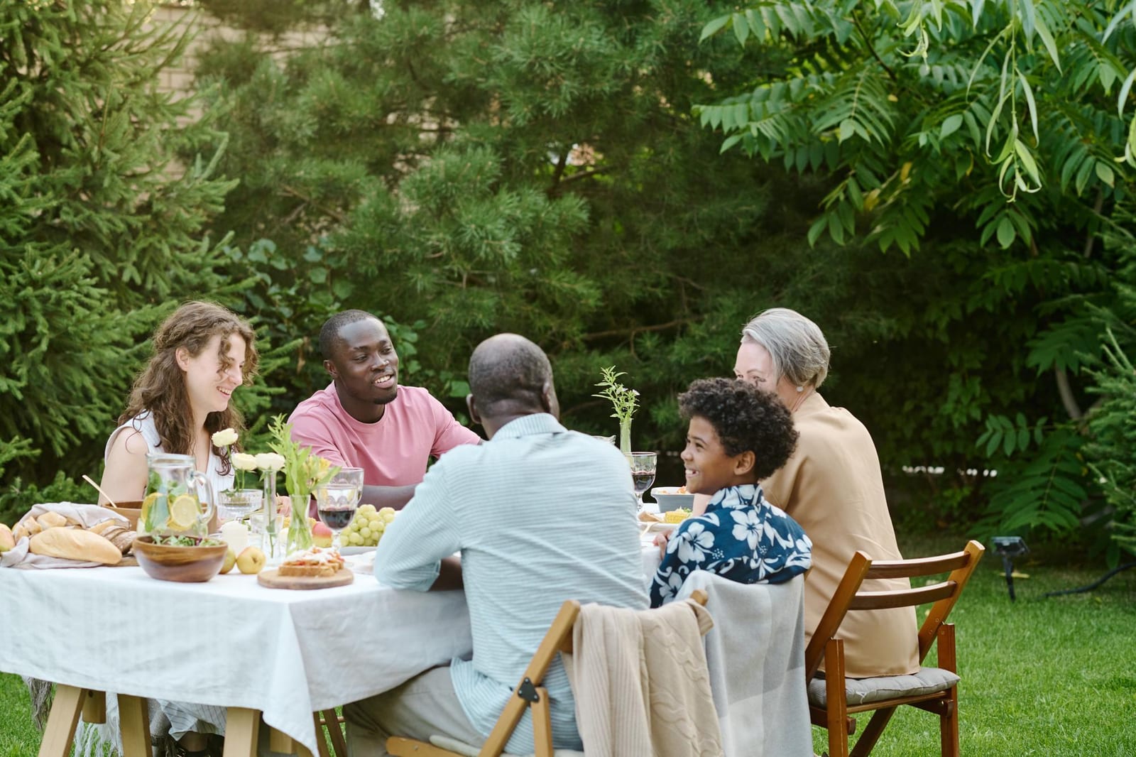 Família reunida à mesa em um quintal arborizado em uma tarde de verão